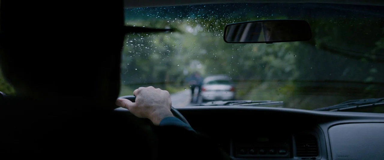 Sinister (2012) movie still: medium — The interior of a car features a dashboard, steering wheel, and rearview mirror. Rain droplets cover the…