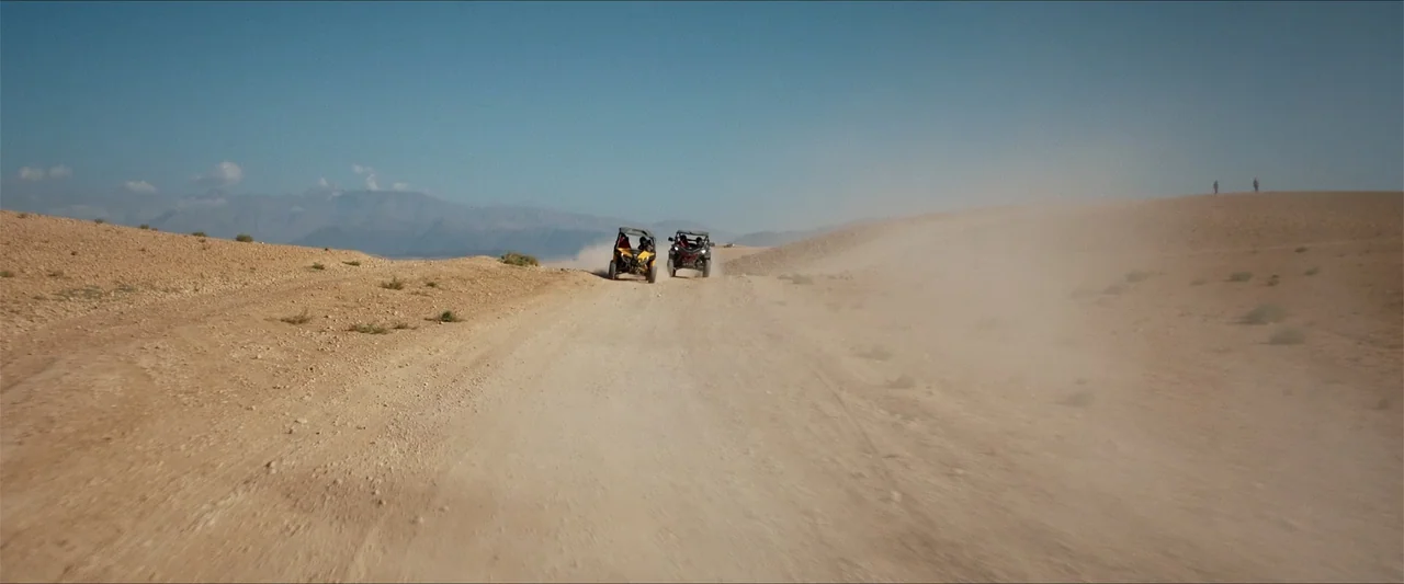 An Endless Wedding (2025) movie still: wide — An arid, sun-baked landscape features a dirt path winding through open, featureless dunes. Two small…