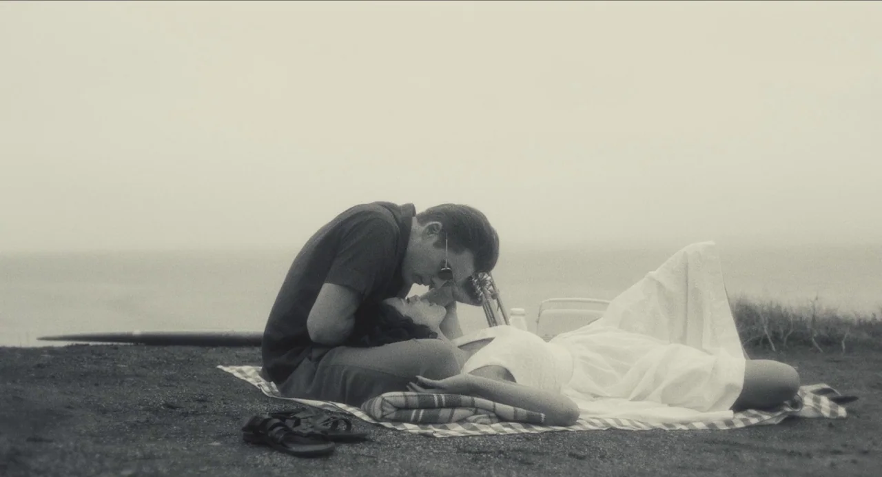 Born To Be Blue (2015) movie still: medium — An overcast cliffside overlooking a muted ocean horizon features a plaid picnic blanket. A man and a…
