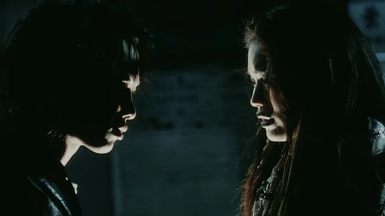 Visible Secret (2001) movie still: medium — Two individuals stand in profile against a pitch-black background in a dark environment. They are…