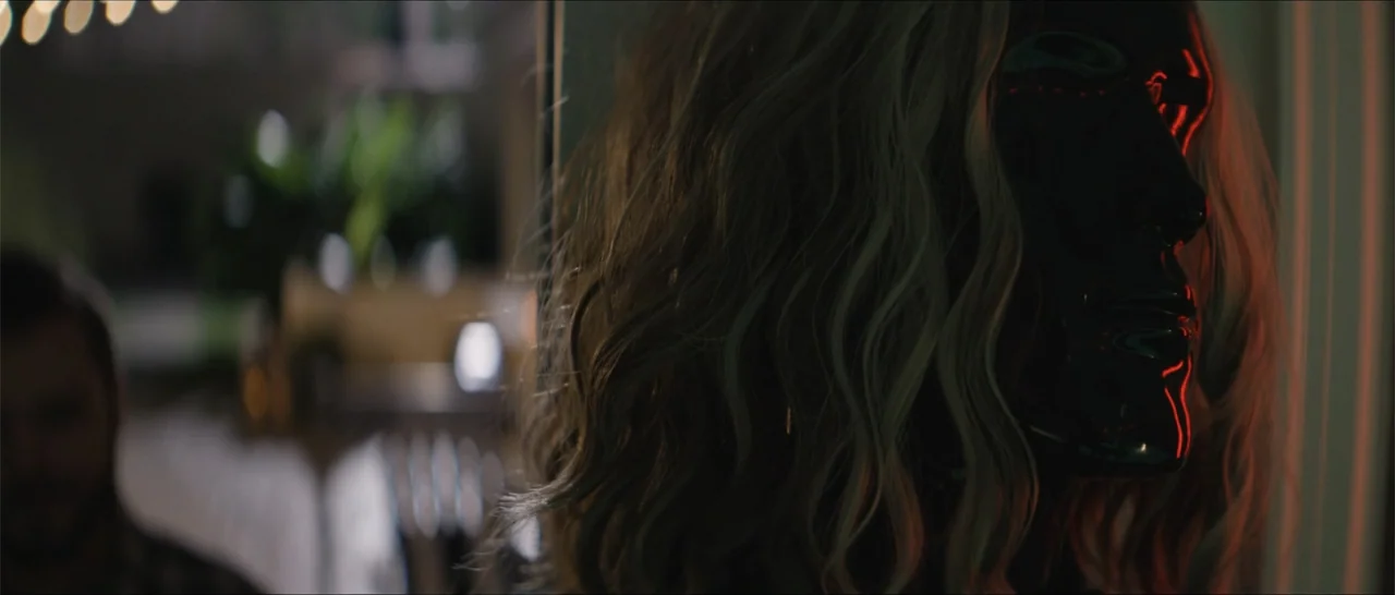 Crescent City (2024) movie still: closeup — A dark indoor space contains a person wearing a shiny dark reflective mask. The subject remains…