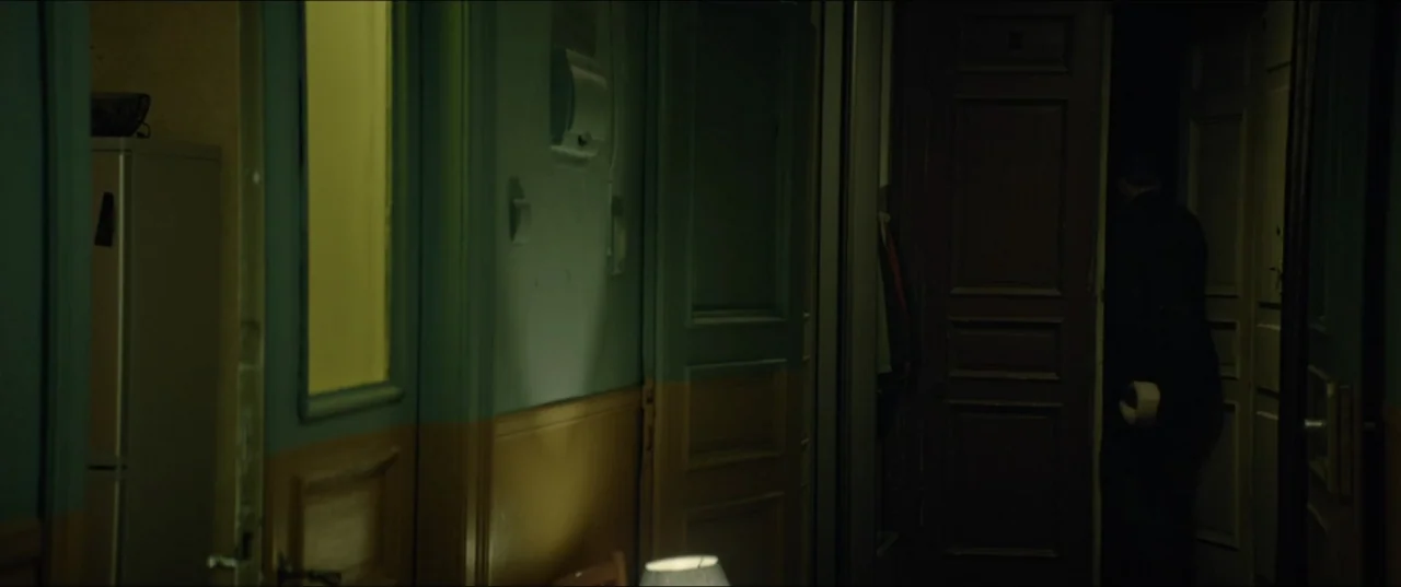 Dogs Don't Wear Pants (2019) movie still: medium — An narrow apartment hallway features two-toned walls with yellow wainscoting and green upper…