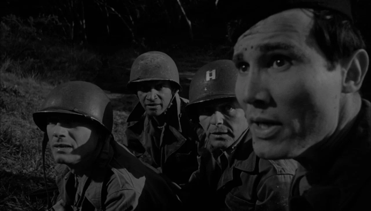 The Manchurian Candidate (1962) movie still: medium — Four soldiers in World War II gear crouch low in a dark, grassy field. They watch an unseen…