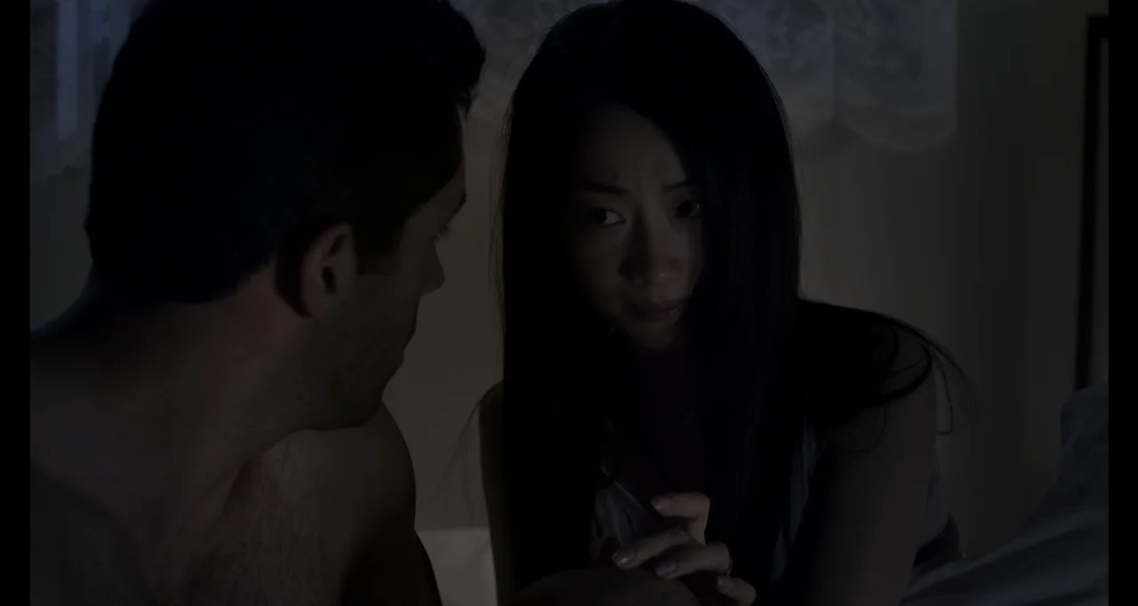 Ninja: Shadow of a Tear (2013) movie still: medium — A dimly lit room with a man and woman in bed at night. They face one another while holding hands.