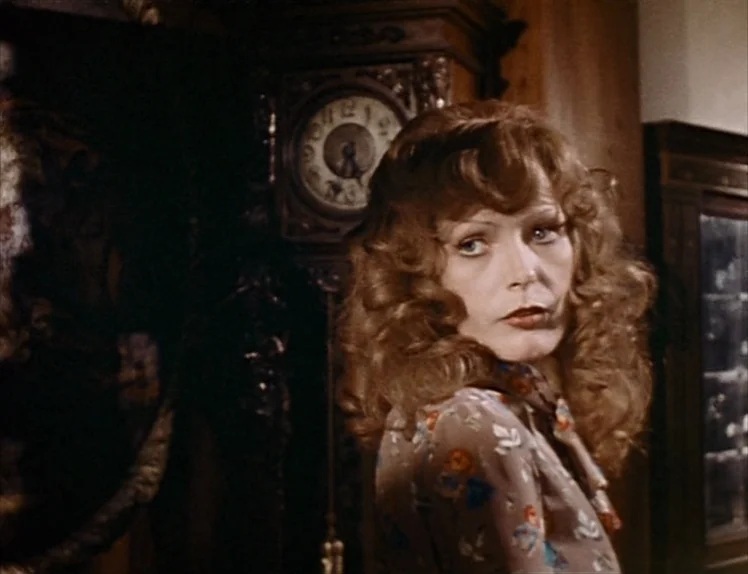 Martha (1974) movie still: medium — A dimly lit room contains an ornate antique standing clock in the background. A woman with reddish-brown wavy…