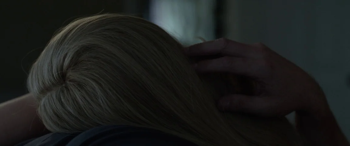 Gone Girl (2014) movie still: closeup — A dimly lit interior space features the back of a person's head. A hand rests on the hair while the…