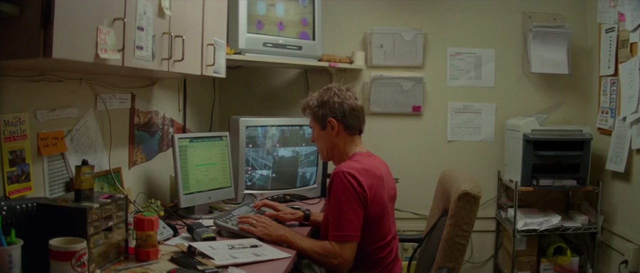 The Florida Project (2017) movie still: medium — A cluttered administrative area features beige cabinets, paper documents, and multiple computer…