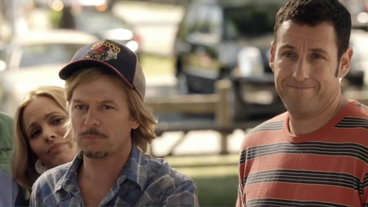 Grown Ups 2 (2013) movie still: medium — A sunny outdoor park area with blurred vehicles visible in the background. Three people stand side by side…