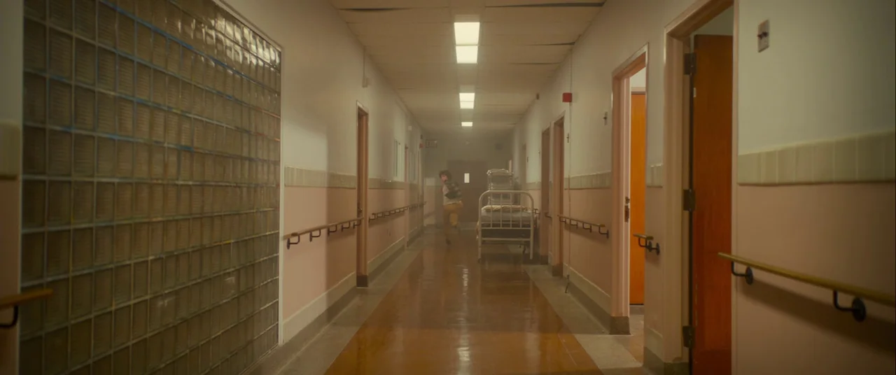 Scary Stories to Tell in the Dark (2019) movie still: wide — A long, dimly lit hospital corridor features pale pink wainscoting and tan vinyl…