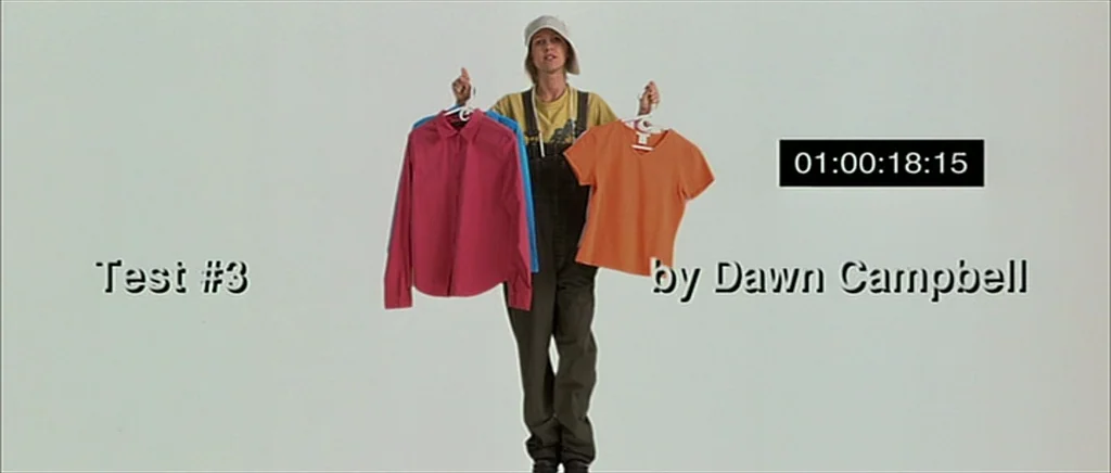 I Heart Huckabees (2004) movie still: fullbody — A woman stands centered against a seamless white studio backdrop in an empty space. She holds a…