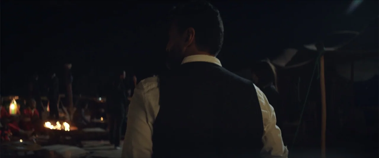 Redemption Day (2021) movie still: medium — An outdoor desert campsite features several people gathered around a glowing campfire at night. A man…