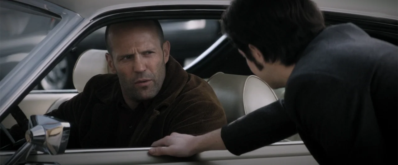Wild Card (2015) movie still: medium — A man sits behind the steering wheel of a vintage car in an urban setting. He speaks to a person leaning into…