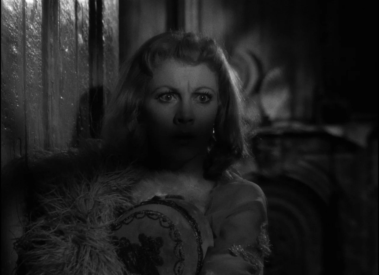 A Streetcar Named Desire (1951) movie still: closeup — A woman stands in a dimly lit, narrow space near a dark vertical surface. She stares toward…