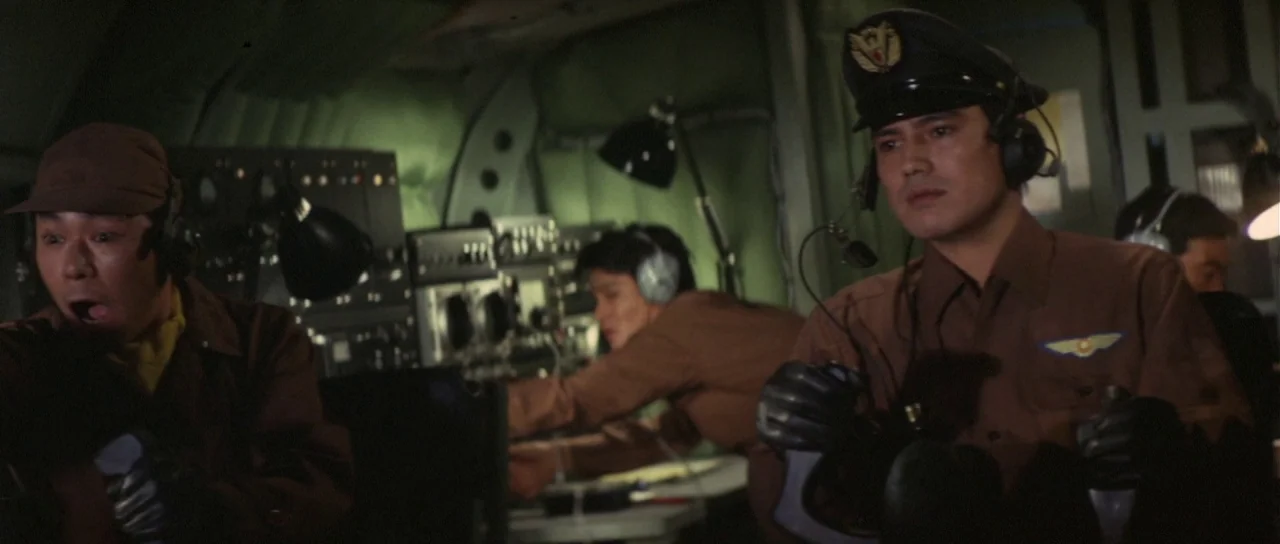 Son of Godzilla (1967) movie still: medium — The interior of a cramped, dimly lit aircraft cockpit with complex navigation equipment. Two pilots in…