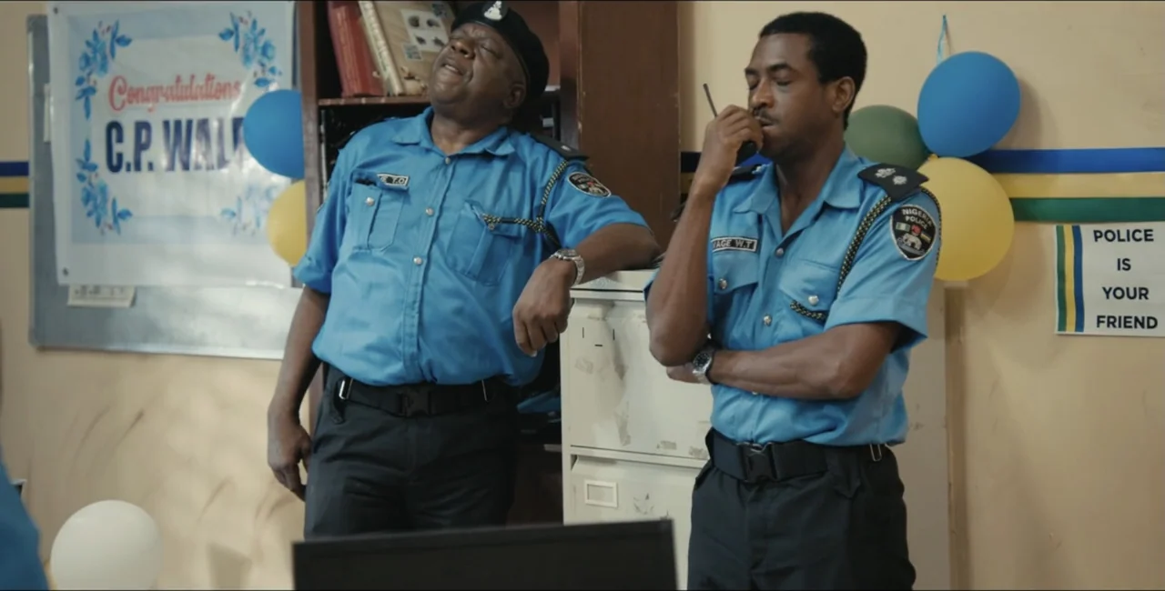 Project Assault (2025) movie still: medium — A police station office wall is adorned with celebratory balloons and signage. Two officers in light…