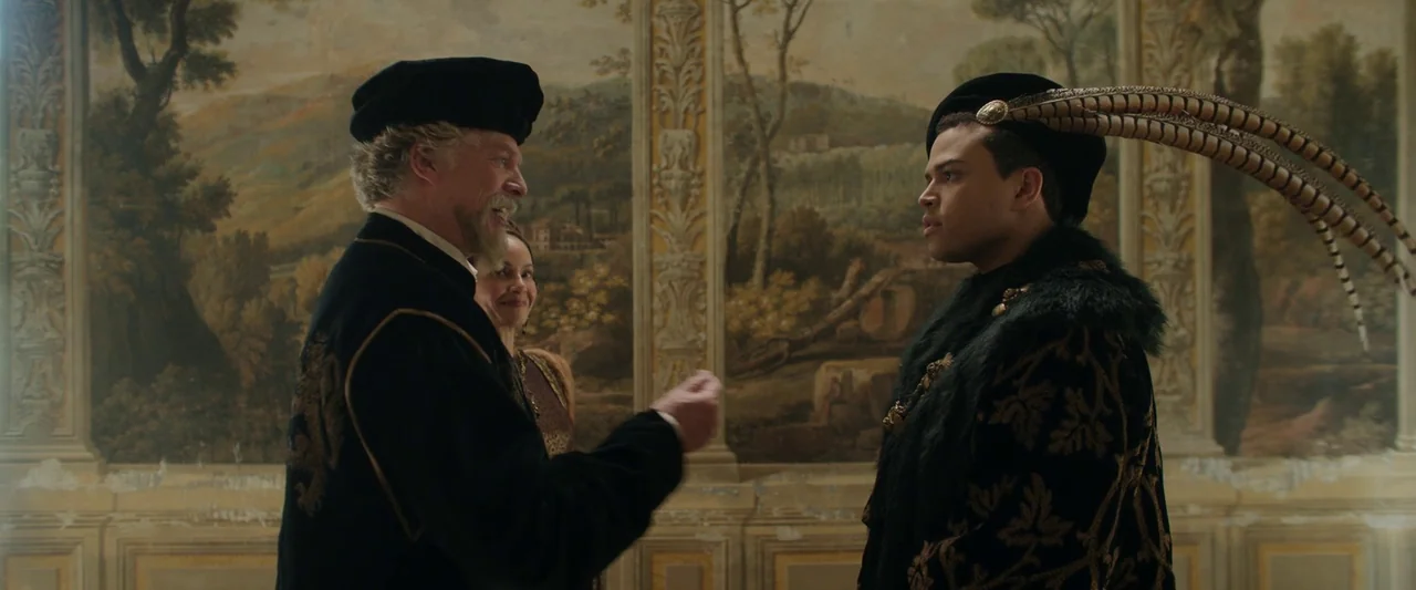 Rosaline (2022) movie still: medium — A room with large wall-mounted landscape paintings depicting Italian-style hills and architecture. An older…