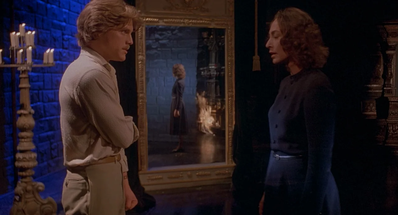 Inferno (1980) movie still: medium — A dark, candlelit room features a large ornate gold-framed mirror on a stone wall. The man and woman face each…