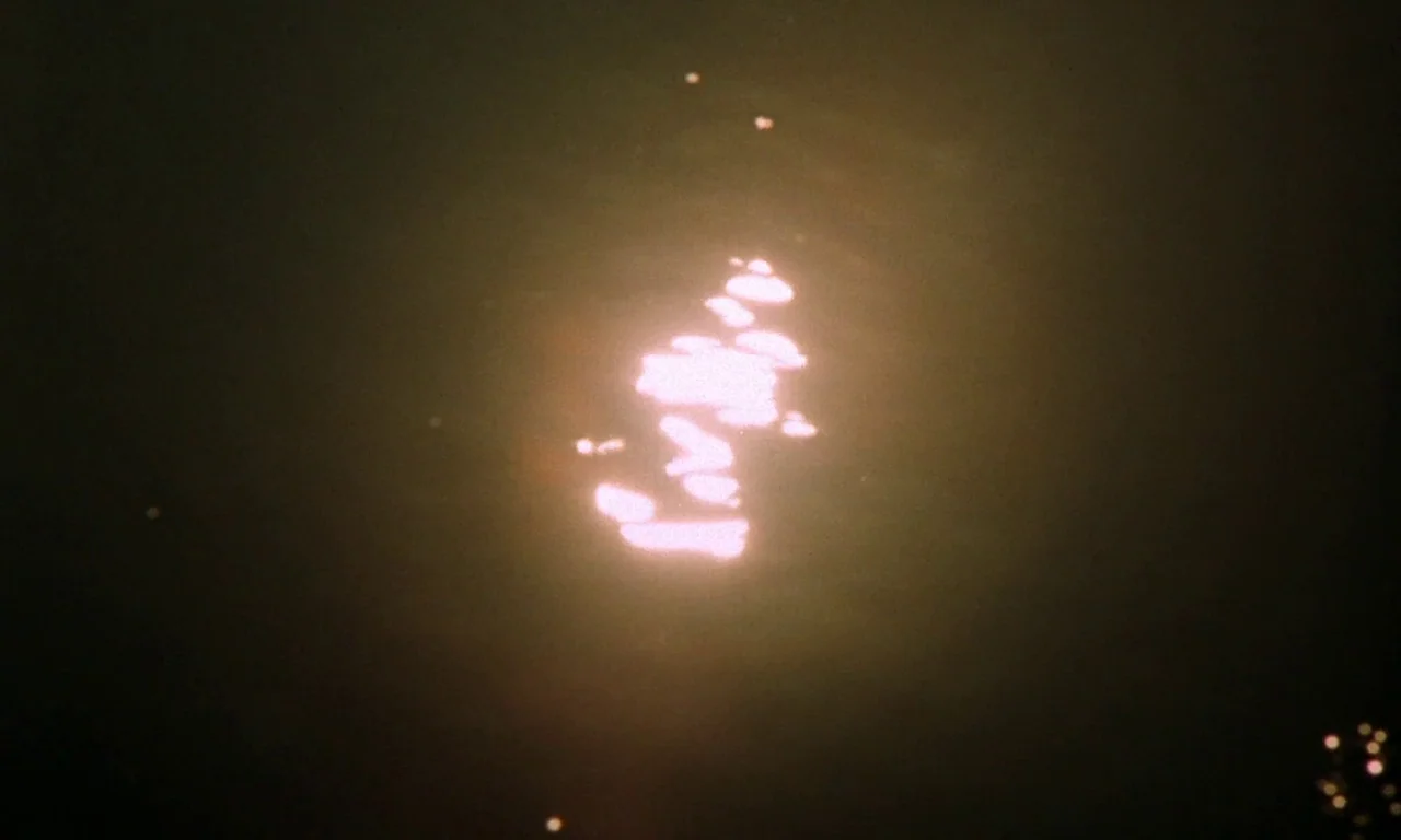 Paganini Horror (1989) movie still: establishing — The frame shows dark, still water at night reflecting a distant light source. Small ripples…
