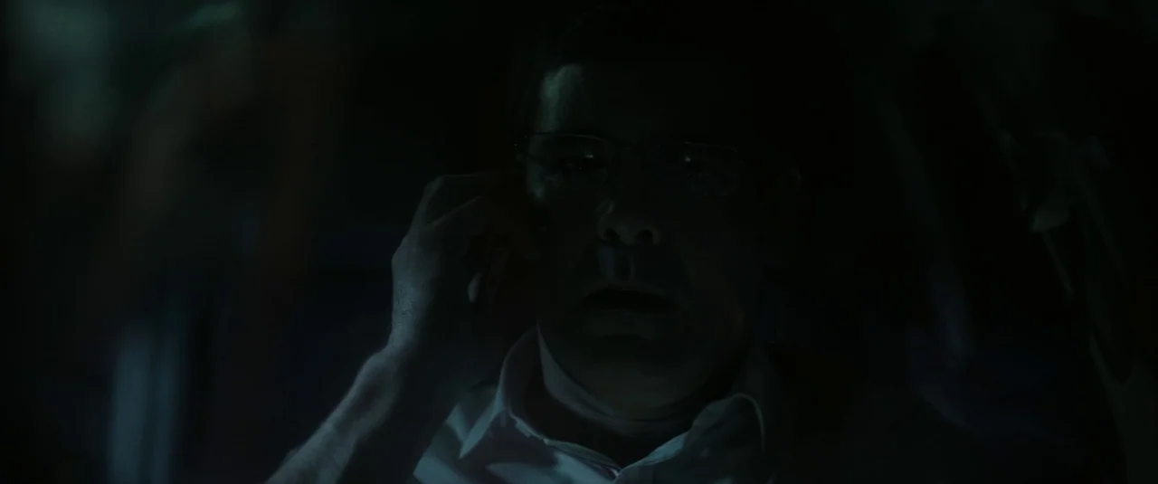 Southbound (2015) movie still: closeup — A man sits inside a dark vehicle cabin at night. He holds a phone to his ear while receiving light from the…