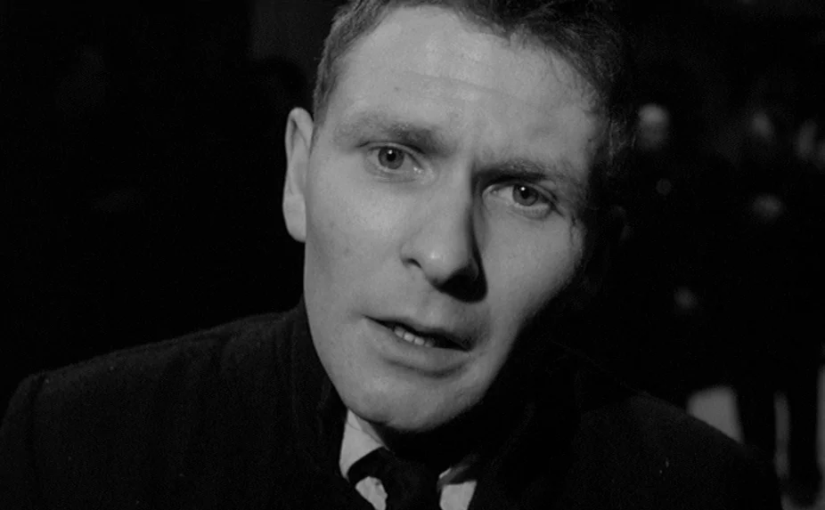 The Criminal (1960) movie still: closeup — A dark night setting with a single man isolated in the frame. The subject looks ahead while standing in…
