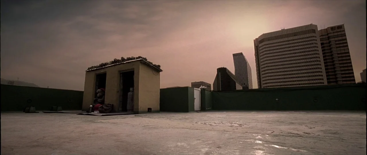 Lady Vengeance (2005) movie still: wide — An expansive concrete rooftop features a small, weathered utility structure against a hazy sky. Modern…