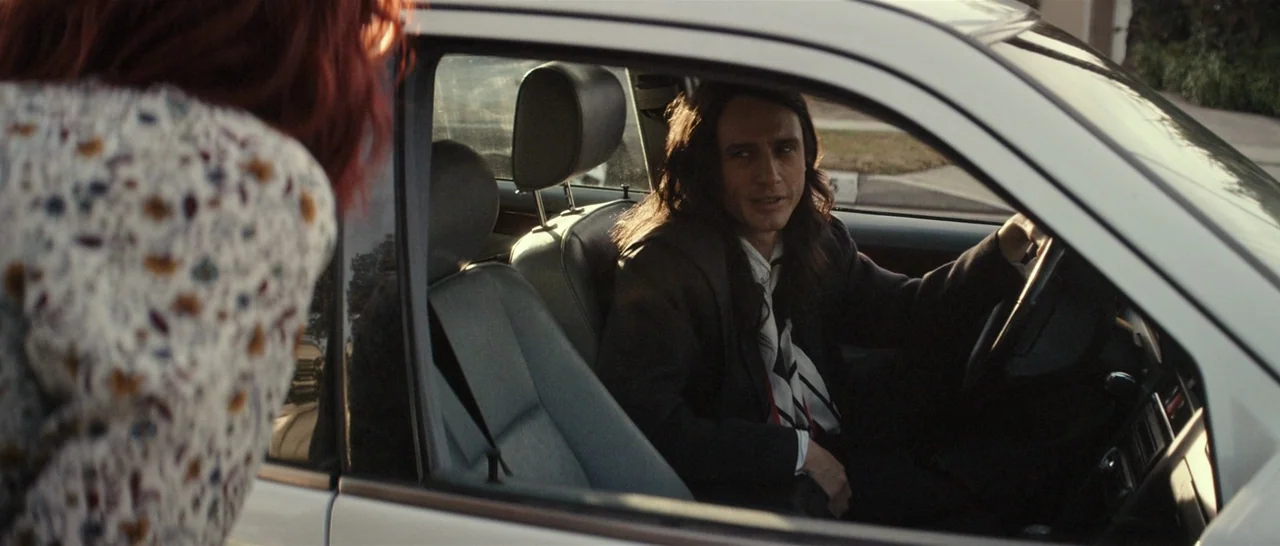 The Disaster Artist (2017) movie still: medium — A man sits in the driver seat of a parked car on a quiet street. He speaks to a woman with reddish…