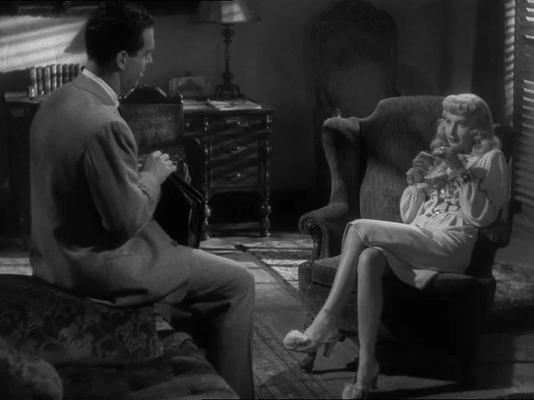 Double Indemnity (1944) movie still: medium — A dimly lit room furnished with a Victorian-style armchair and a heavy desk lamp. A man in a suit…