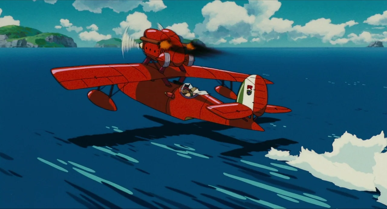 Porco Rosso (1992) movie still: wide — A bright red biplane flies low over the deep blue ocean water. White spray curls from the surface beneath the…