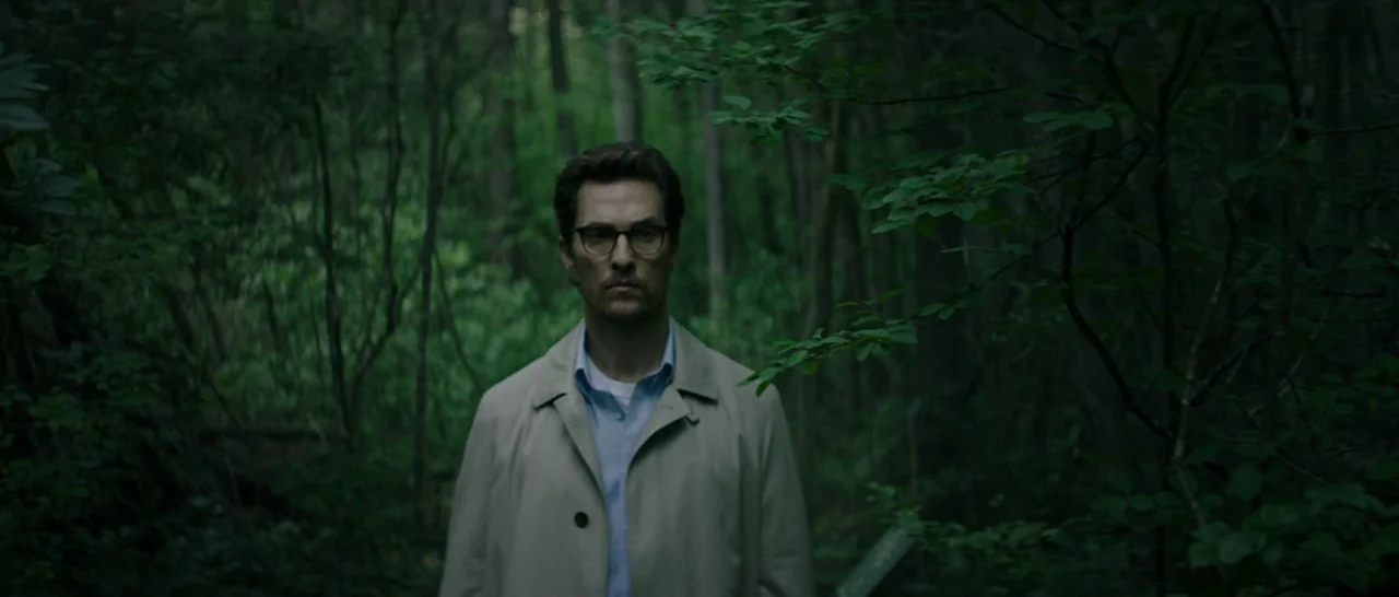 The Sea of Trees (2015) movie still: medium — A dense, overgrown patch of woods with thick foliage obscuring the surrounding trees. A man in a beige…