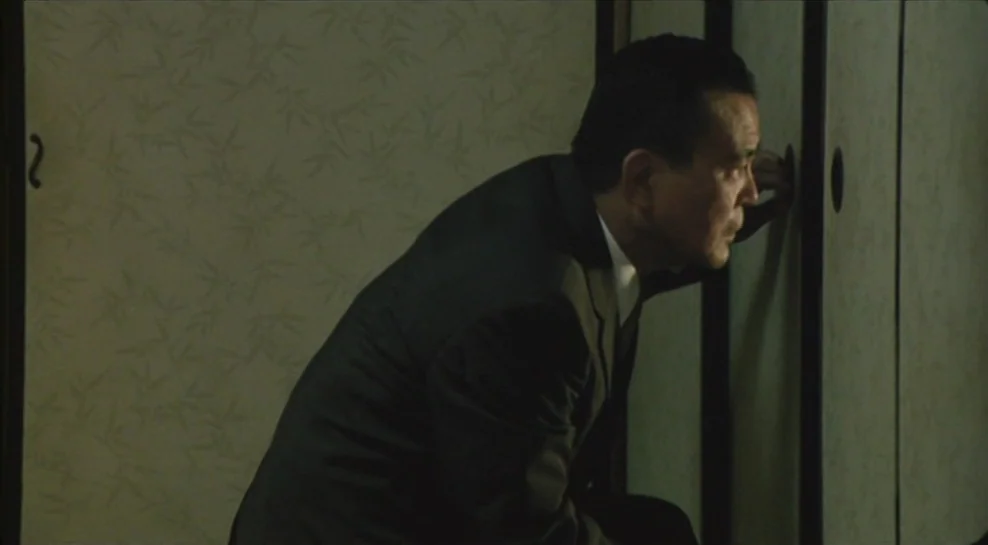 Madadayo (1993) movie still: medium — A traditional room features sliding fusuma doors with pale, patterned paper panels. A man in a suit crouches…