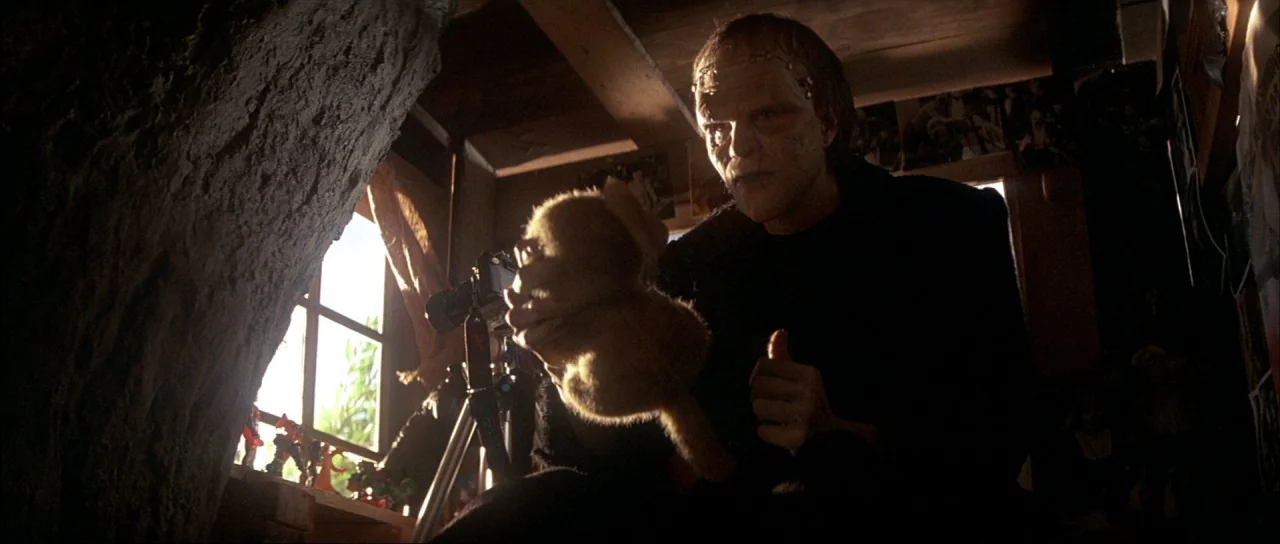 The Monster Squad (1987) movie still: medium — A dimly lit room with wooden walls and a window overlooking greenery. A pale man with surgical scars…