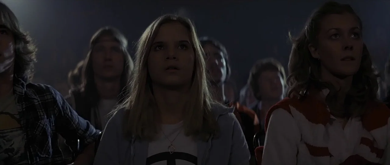 Pink Floyd The Wall (1982) movie still: medium — Rows of young people sit in a dark room illuminated from the front. The audience stares ahead at a…