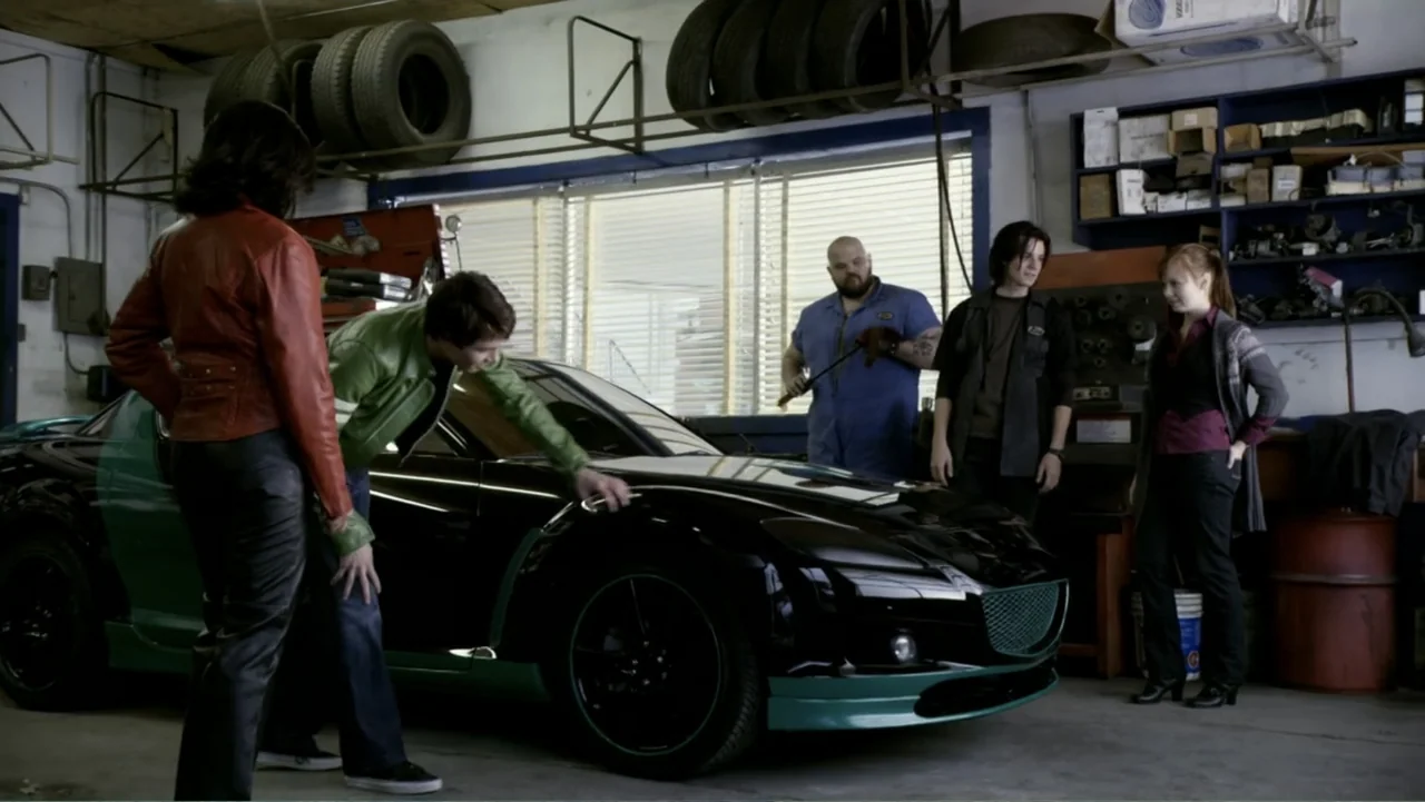 Ben 10: Race Against Time (2008) movie still: medium — A cluttered mechanic shop features tires hanging on walls and shelves filled with parts. Four…