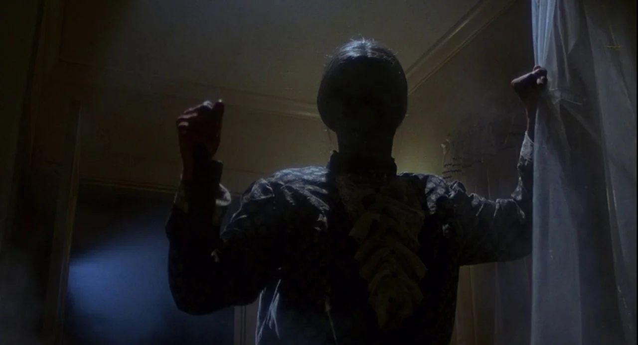 Psycho III (1986) movie still: medium — A dimly lit room features a person in silhouette standing before a thin curtain. The figure grasps the…