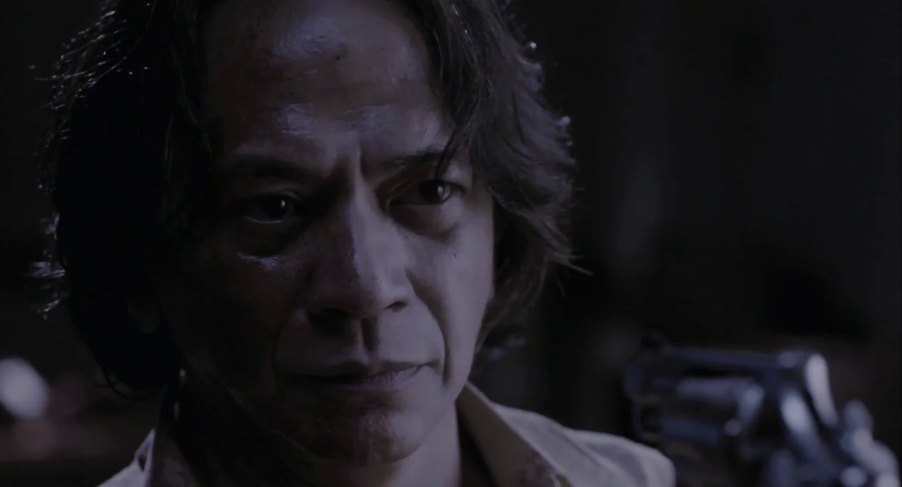 The Raid (2012) movie still: closeup — A dimly lit, shadowed space provides a stark backdrop for the close-up shot. A man in his fifties looks…