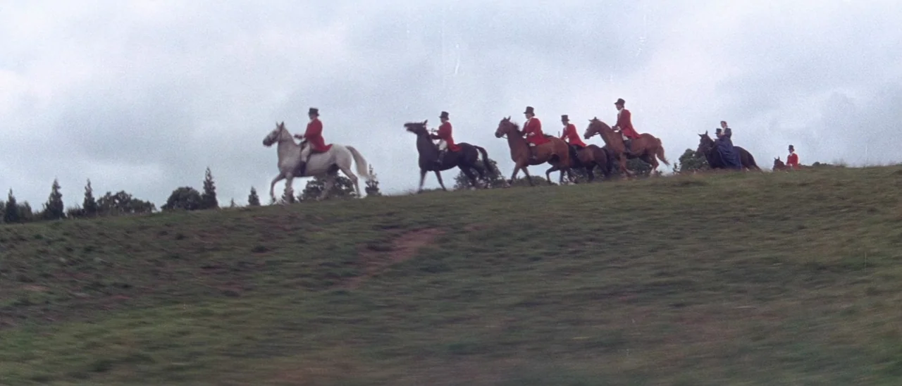 The Tomb of Ligeia (1964) movie still: wide — A group of equestrians ride horses across the crest of a grassy hill. The overcast sky is flat and…