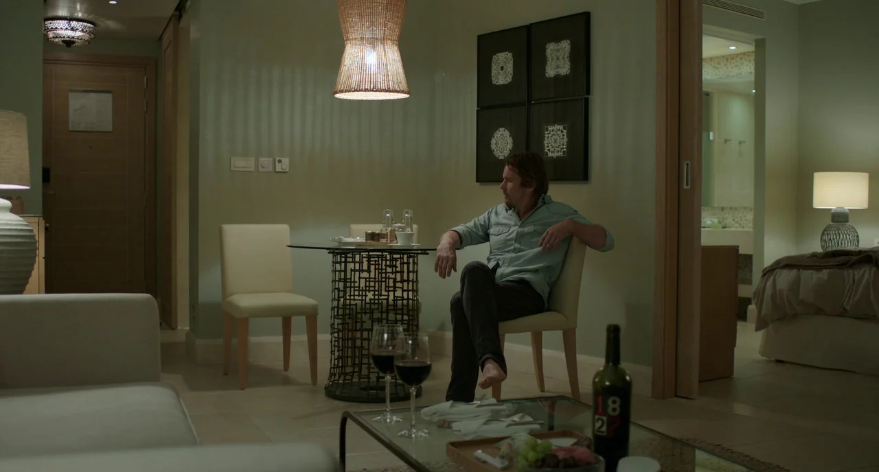 Before Midnight (2013) movie still: wide — A modern hotel room features pale green walls, a wicker pendant light, and furniture. A man sits alone on…