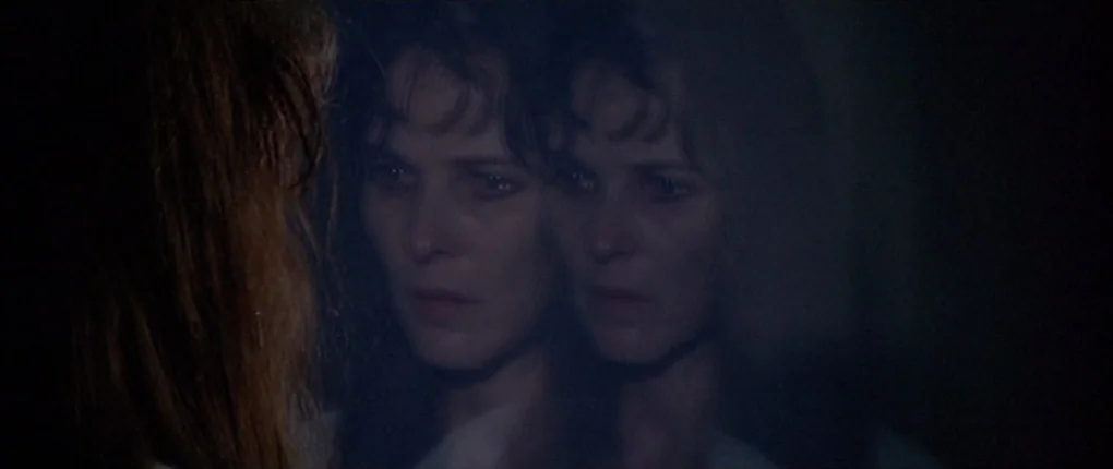 3 Women (1977) movie still: closeup — A dark, dimly lit bathroom space with reflective surfaces. A woman observes her own reflection in a mirror.