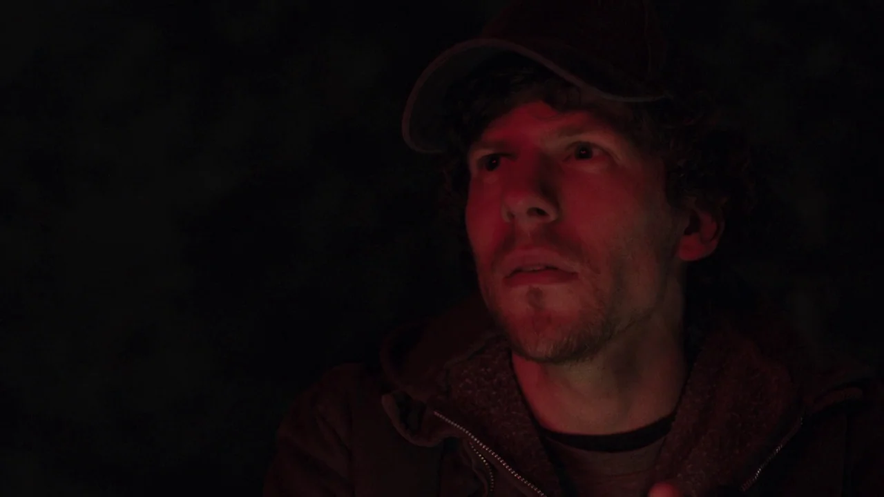 Night Moves (2013) movie still: closeup — A dark outdoor setting at night with no visible background features. A man is illuminated by intense red…