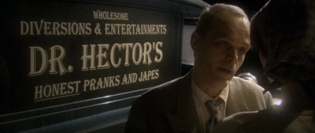 Manderlay (2005) movie still: medium — A dark, dimly lit alleyway at night features the side of a delivery truck. A middle-aged man in a tan suit…