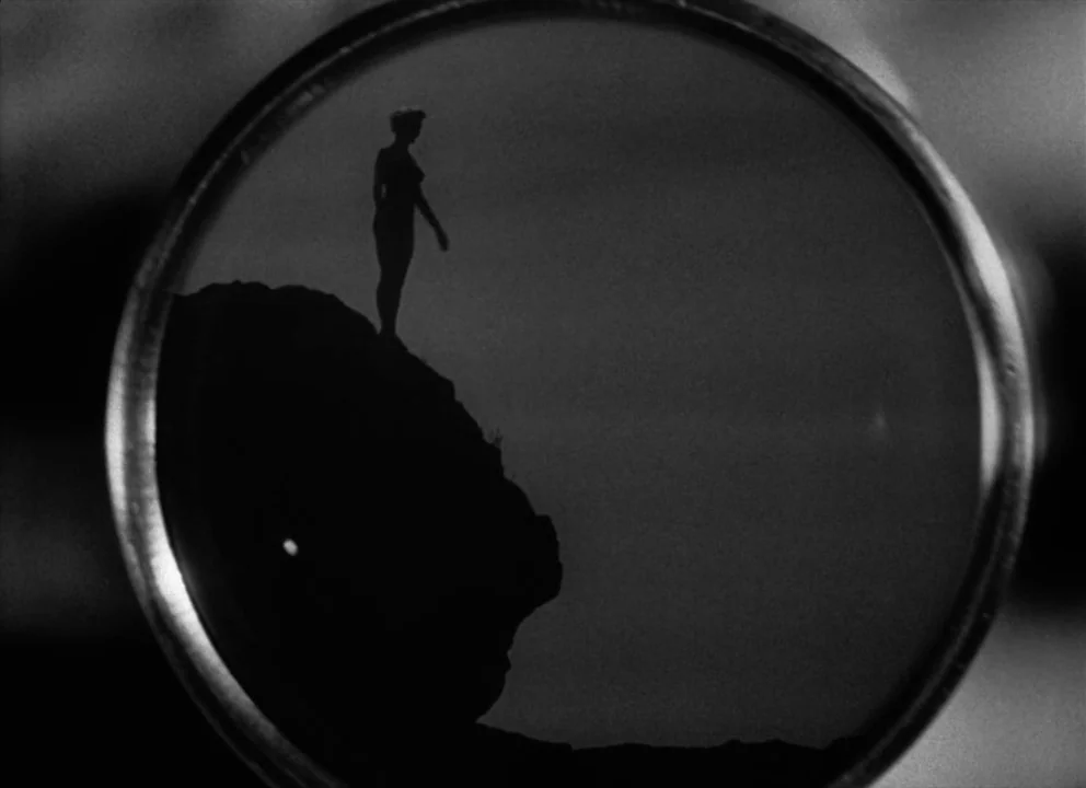 The Lady from Shanghai (1947) movie still: wide — A dark rocky cliff edge seen through a circular aperture. A lone figure stands on the top of the…