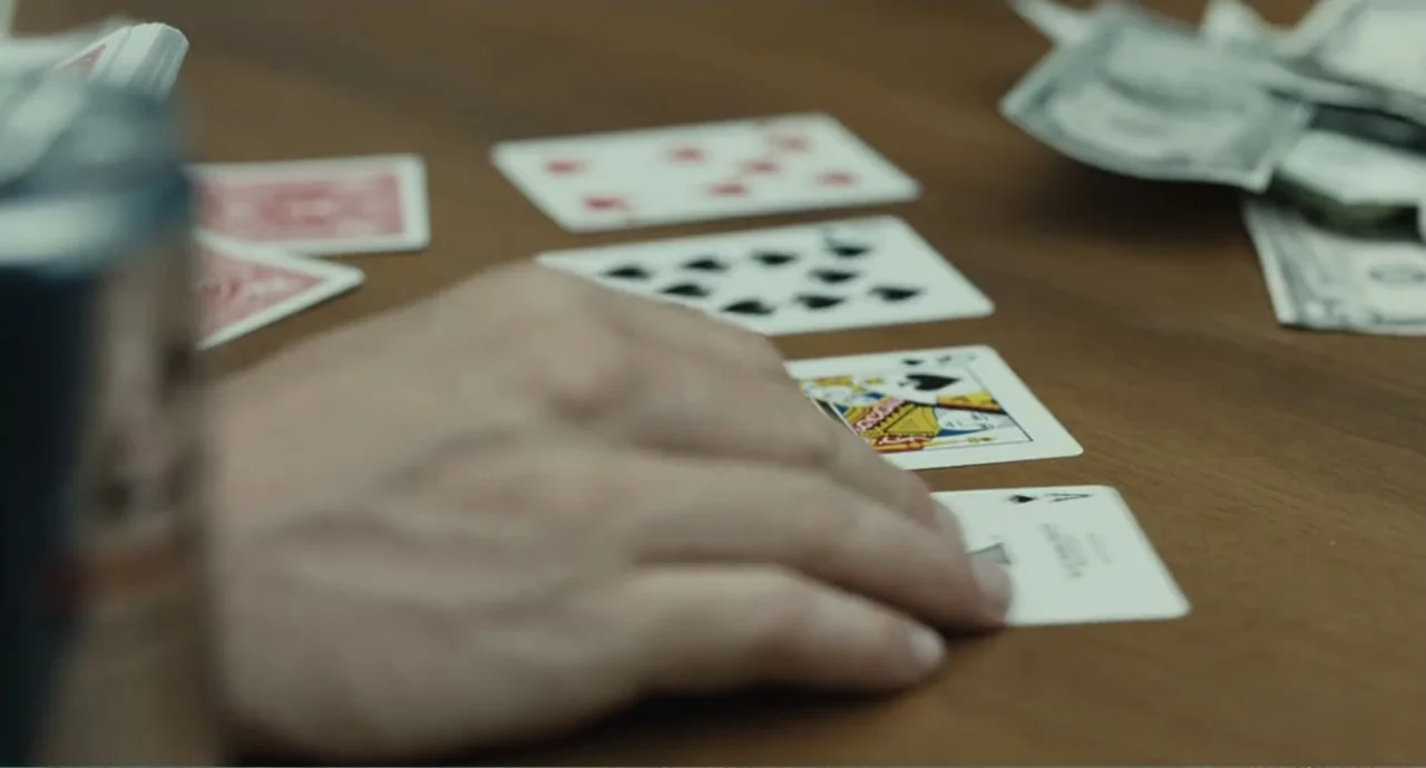 Bad Boys: A True Story (2003) movie still: closeup — A wooden table surface features scattered playing cards and a stack of paper currency. A blurry…