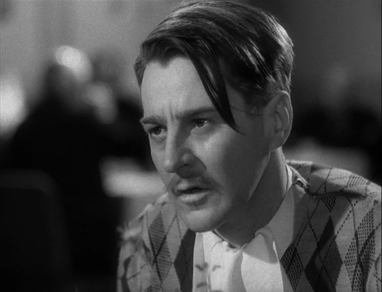 Music in Darkness (1948) movie still: closeup — An interior space with a blurred, indistinct background of an unknown setting. A man in an argyle…