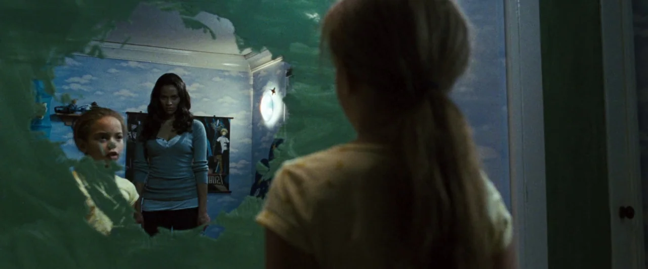 Mirrors (2008) movie still: medium — A child observes her own reflection and a woman behind her in a mirror. The wall behind them is decorated with…