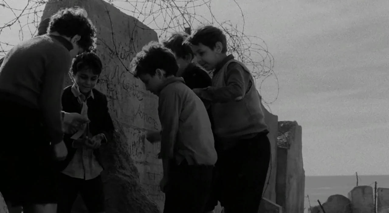 The Great Beauty (2013) movie still: medium — A group of children gather against a damaged stone wall topped with barbed wire. Several young boys…