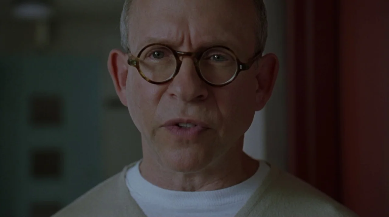 Lady in the Water (2006) movie still: closeup — A man stands in a dimly lit hallway with muted walls. The man looks directly into the camera while…