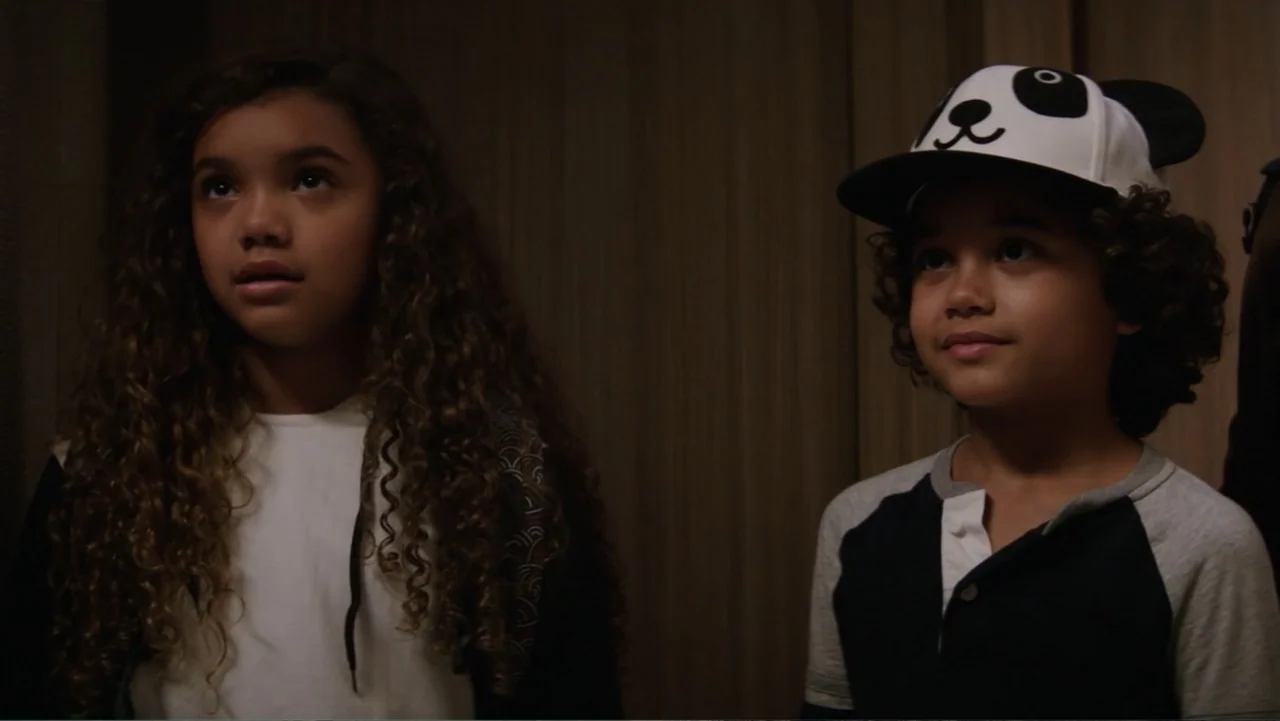 Skyscraper (2018) movie still: medium — A dimly lit indoor corridor with wooden paneled walls. A young girl and a young boy stand side by side…