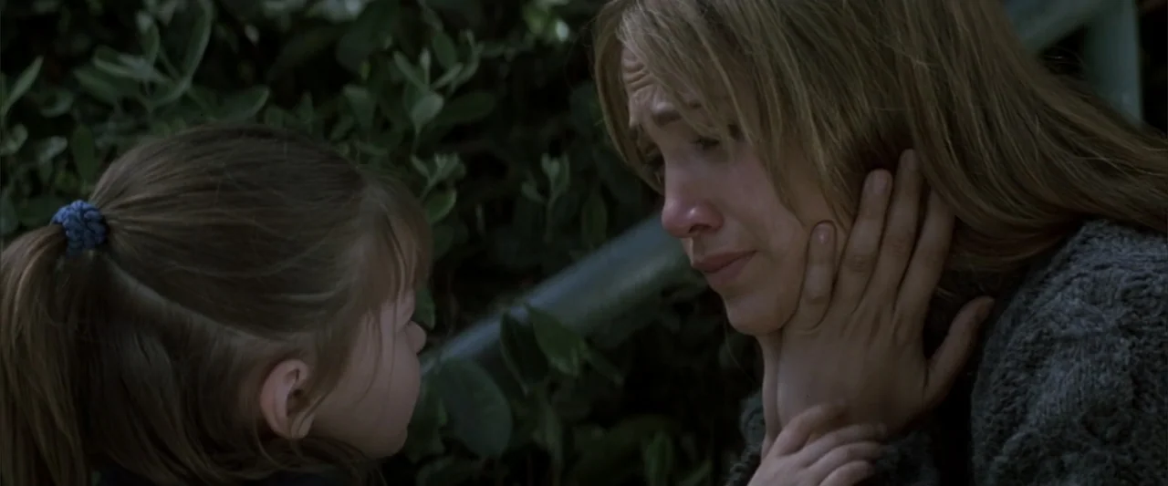 Enough (2002) movie still: medium — A woman and a child are positioned near lush green bushes outdoors. A young girl reaches out to touch the…