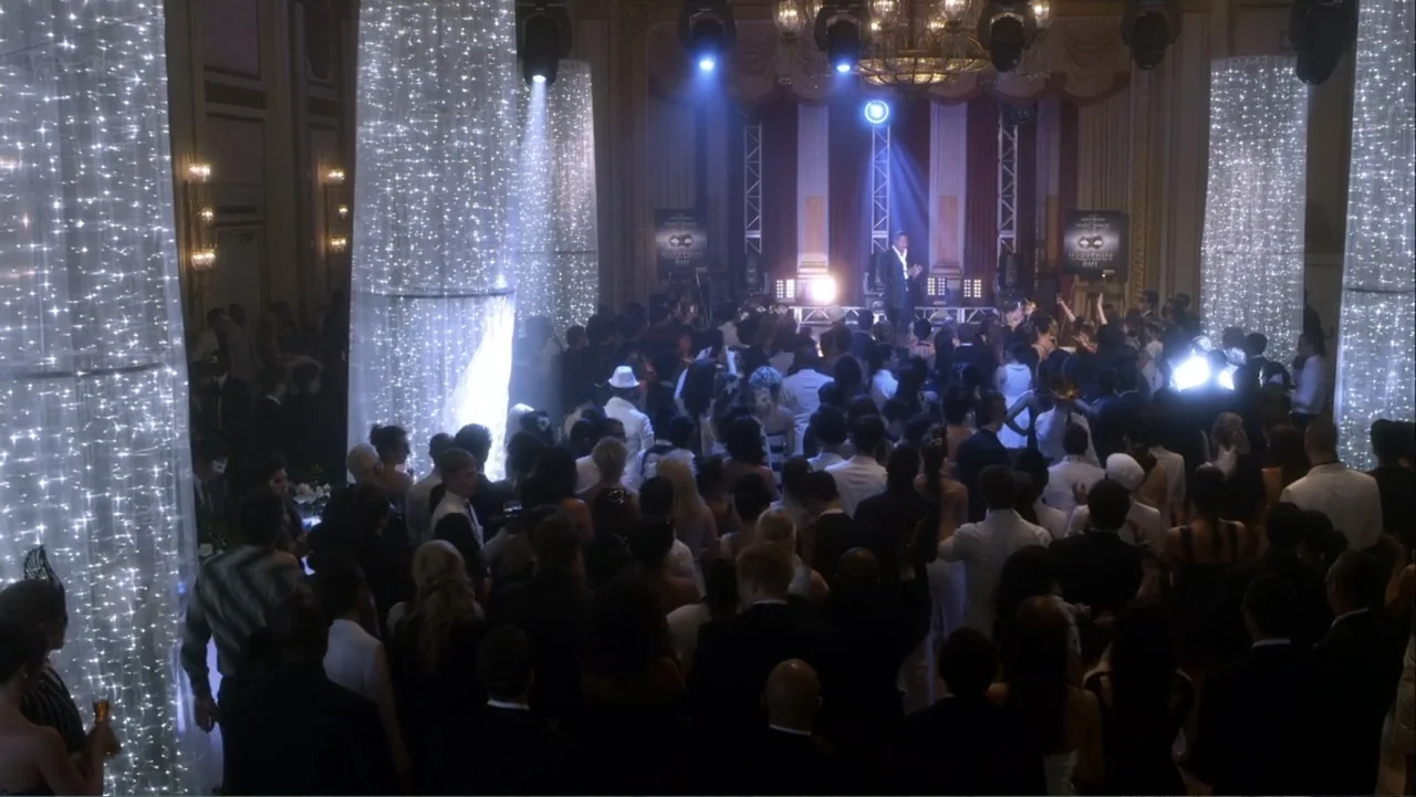 Rags (2012) movie still: wide — A crowded ballroom features a central stage and multiple towering pillars covered in twinkling lights. A large crowd…