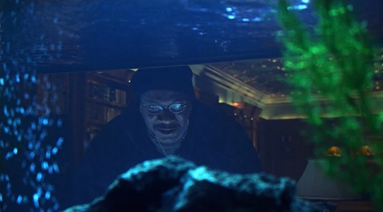 Out Of Sight (1998) movie still: medium — A man looks through the glass of an aquarium into a dimly lit library. The blue water light hits his face…